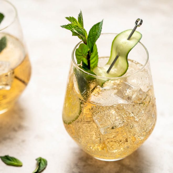 a clear blass with ice, liquid and a garnish is backlit from behind
