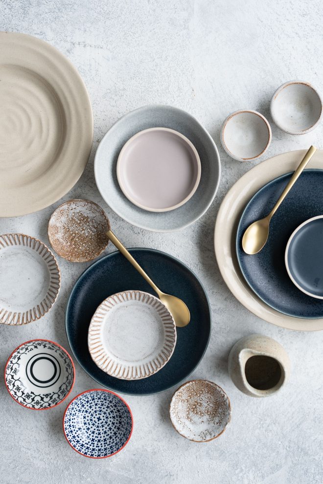 Image of handmade and hand-painted plates, cups, and bowls on a white counter space. photograph by Lauren Caris Short of Food Photography Academy