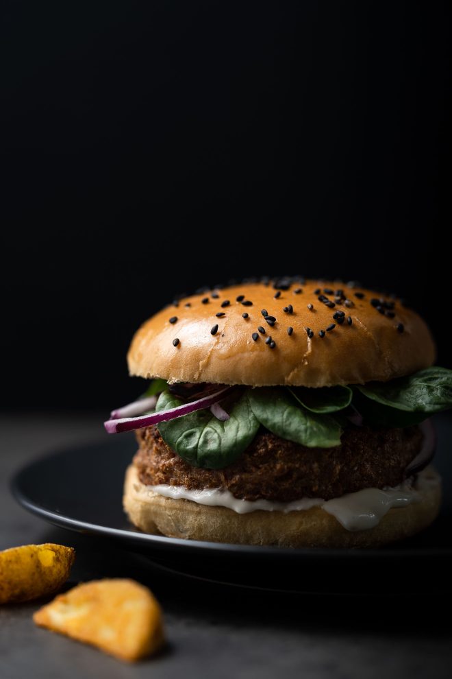 A cheeseburger in front of a black backdrop. Photograph by Lauren Caris Short of Food Photography Academy.