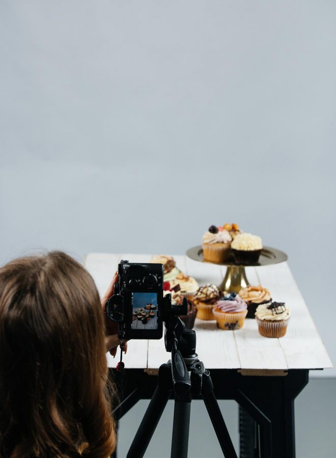 Lauren Short, a professional food photographer and educator, stands behind her camera tripod as she photographs some cupcakes a table.