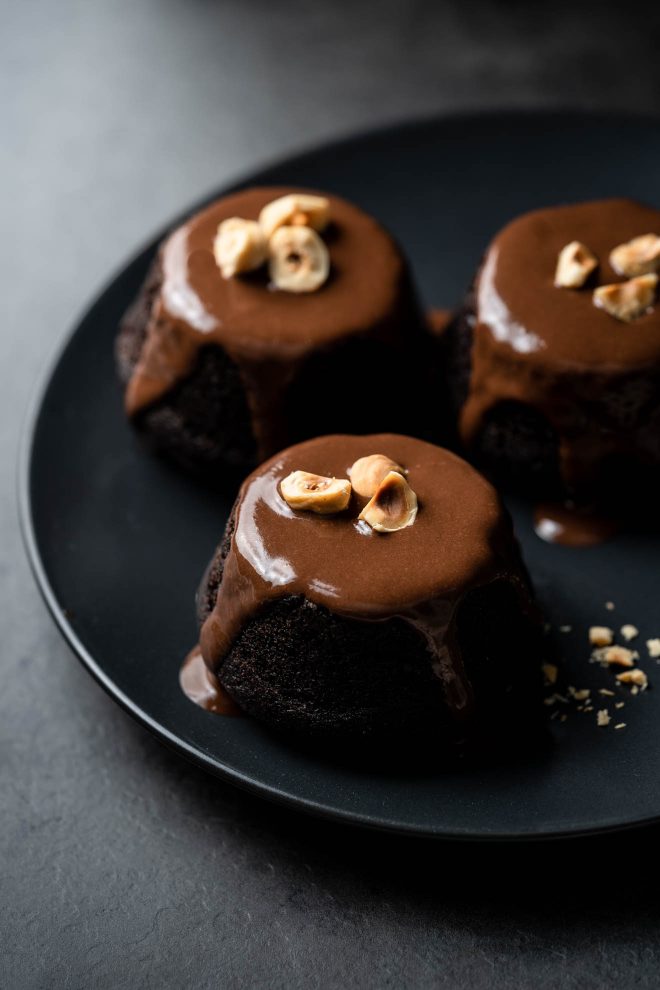 three mini chocolate cakes on a plate. Each cake has chocolate sauce poured over it. Photo by Lauren Caris Short of Food Photography Academy.