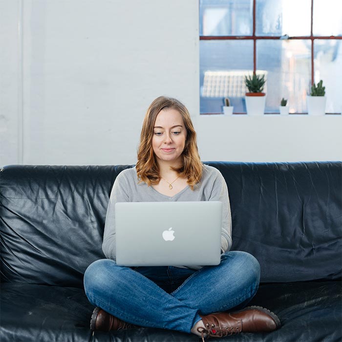 a woman sits on a couch with her legs folded and her laptop in her lap