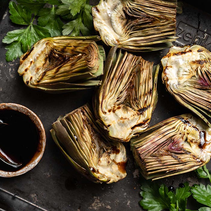 several grilled artichokes lie on a surface
