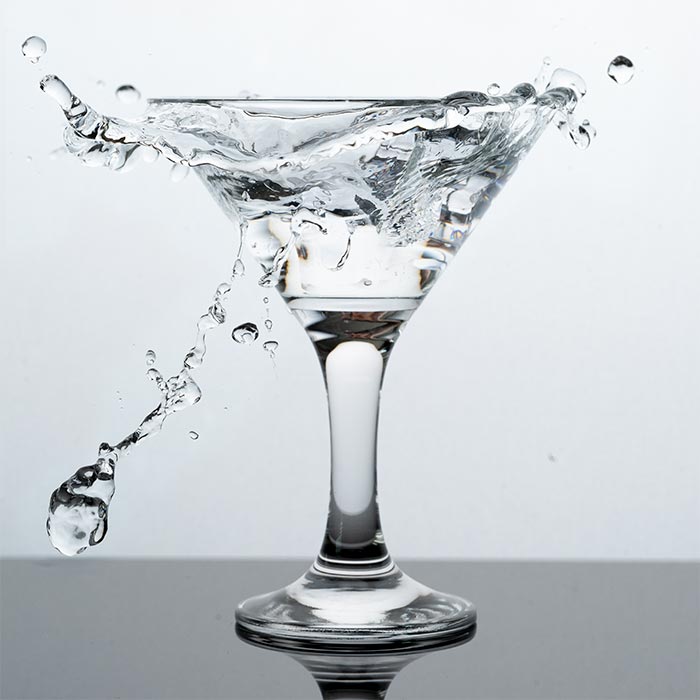 a martinie glass filled with a clear liquid splashes onto the countertop