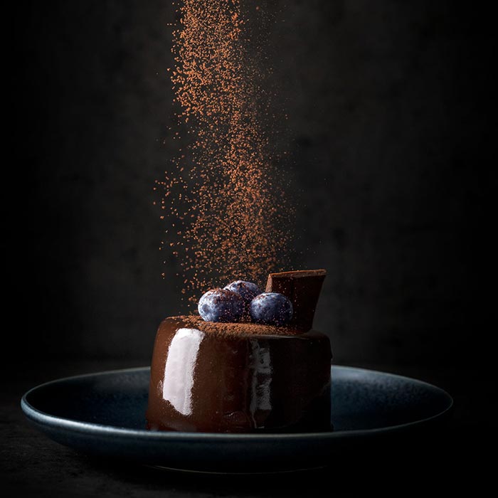 a chocolate dessert sits on a plate while chocolate powder is being sprinkled on it