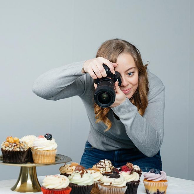 Lauren Caris Short hold her camera to her eye as she takes a picture of food