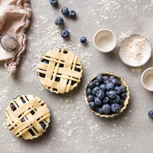 several blue berry pies are displayed while other ingredients are strone about