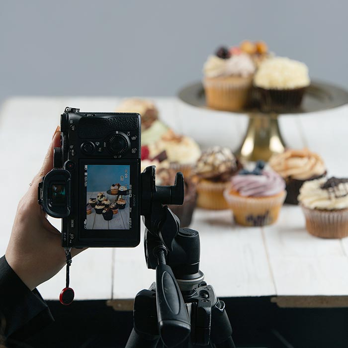 a photographer holds up their camera so you can see the display screen while a table in the background has various food items displayed on it