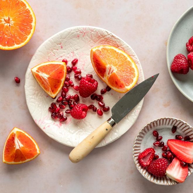 pieces of a cut up orange sit on a white plate along with a knife and berries