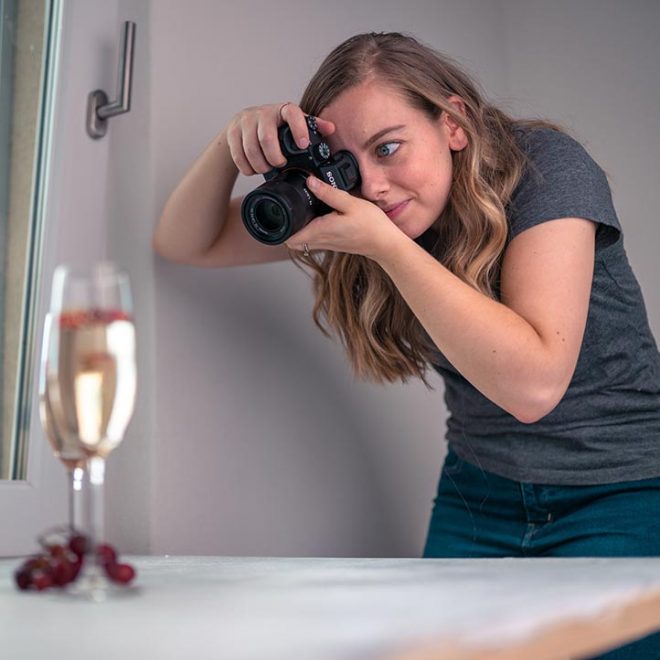 a woman holds a camera to here eye to take a picture of a glass