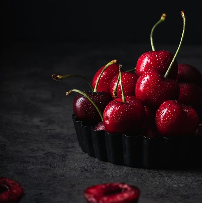 A small mountain of cherries rests in a tray with an easy dark and moody lighting setup by Lauren Short from Food Photography Academy.