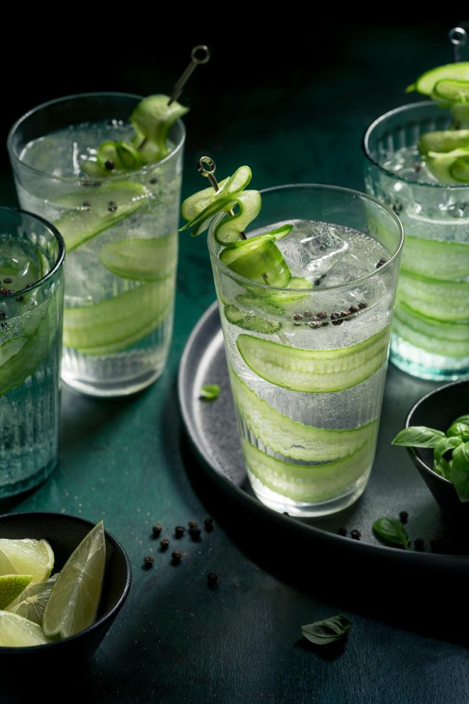 Glasses of gin and tonic with cucumber slices rest on a black tray